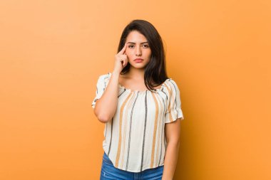 Genç, kıvrımlı bir kadın şakağı parmağıyla işaret ediyor, düşünüyor, bir işe odaklanıyor..