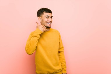 Genç İspanyol adam parmakları ile bir cep telefonu arama jesti gösteren.