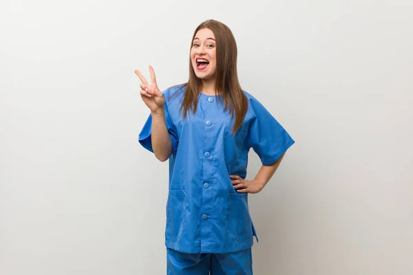 Junge Krankenschwester Vor Einer Weißen Wand Mit Siegeszeichen Und Breitem — Stockfoto