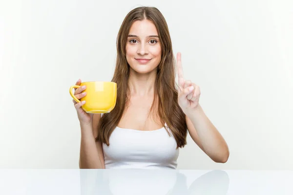 指でナンバーワンを示すカップを持つ若い白人女性 — ストック写真