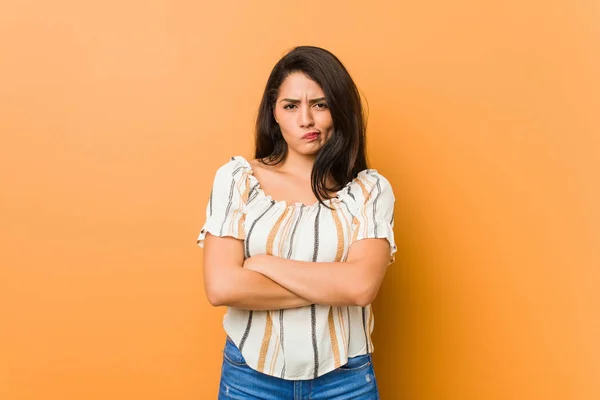 Young curvy woman frowning face in displeasure, keeps arms folded.