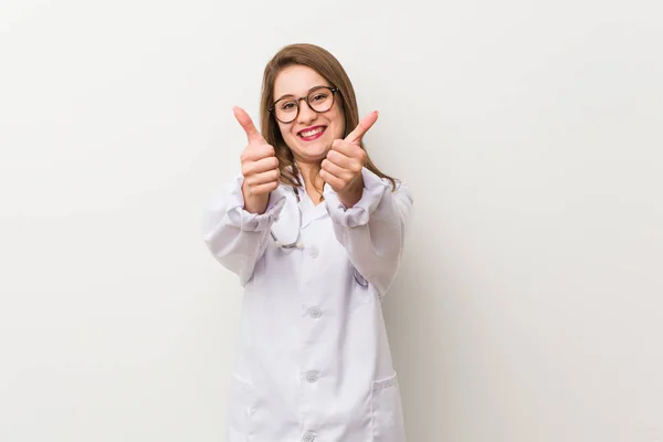 Jonge Dokter Vrouw Tegen Een Witte Muur Met Duimen Ups — Stockfoto