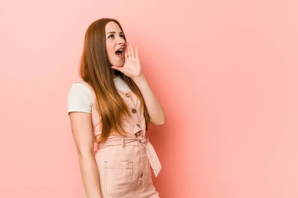 Young ginger woman with freckles shouting and holding palm near opened mouth.