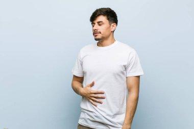 Beyaz bir tshirt giyen genç beyaz adam karın dokunur, hafifçe gülümsüyor, yeme ve memnuniyet kavramı.