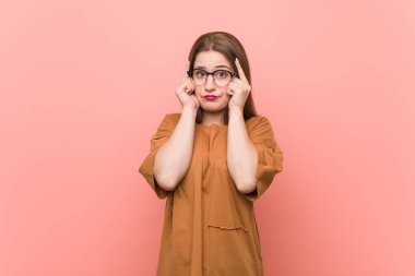 Gözlük takan genç öğrenci kadın bir göreve odaklanmış, işaret parmaklarını başını işaret eden bir göreve odaklanmıştır..