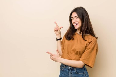 Genç esmer kadın bir kopya alanı için ön parmaklar ile işaret bej arka plan karşı, heyecan ve arzu ifade.