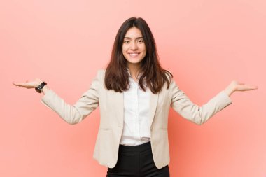 Pembe bir arka plan karşı Genç esmer iş kadını kolları ile ölçek yapar, mutlu ve kendinden emin hissediyor.