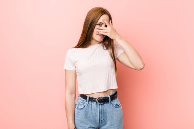 Pembe bir duvara karşı genç kızıl saçlı kadın parmakları ile kamera yanıp söner, yüz kapsayan utandım.