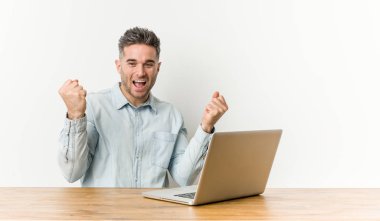 Genç yakışıklı adam onun laptop ile çalışan kaygısız ve heyecanlı tezahürat. Zafer kavramı.