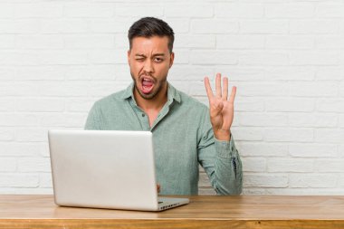 Genç filipinli adam dizüstü bilgisayar ile çalışan oturan bir göz göz kırpıyor ve el ile tamam bir jest tutar.