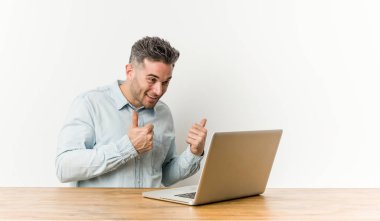 Young handsome man working with his laptop raising both thumbs up, smiling and confident. clipart
