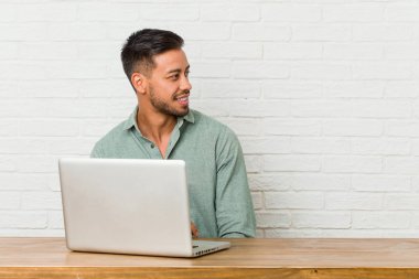 Genç filipinli adam dizüstü bilgisayar ile çalışan oturan bir kenara gülümseyen, neşeli ve hoş görünüyor.