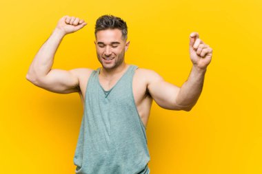 Özel bir gün kutlayan sarı bir arka plan karşı Genç fitness adam, atlar ve enerji ile silah yükseltmek.