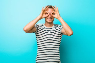 Gözleri üzerinde tamam işareti gösteren mavi bir duvara karşı genç beyaz adam