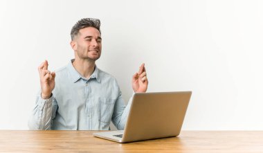 Genç yakışıklı adam şans için parmakları geçiş dizüstü bilgisayar ile çalışıyor