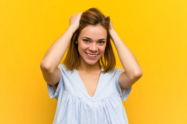 Young pretty young woman laughs joyfully keeping hands on head. Happiness concept.