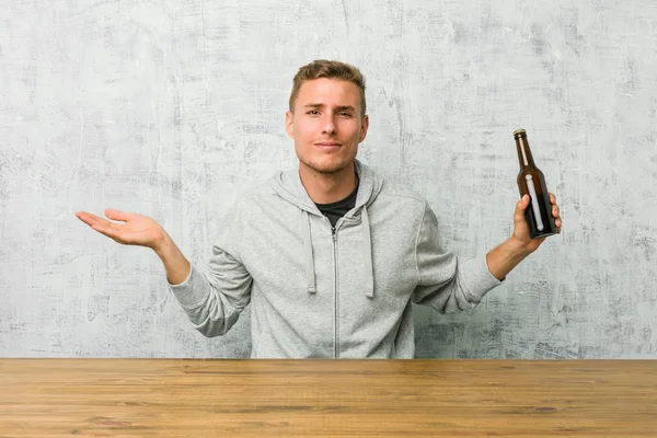 Jonge Man Drinken Van Een Biertje Een Tafel Twijfelen Afschudden — Stockfoto