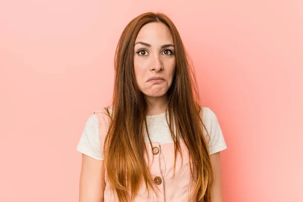 Young ginger woman with freckles shrugs shoulders and open eyes confused.