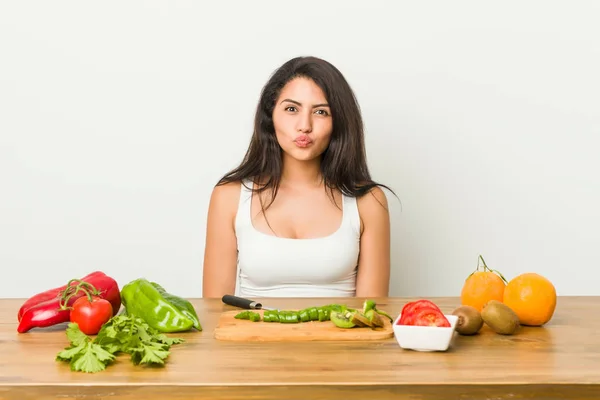 Young curvy woman preparing a healthy meal blows cheeks, has tired expression. Facial expression concept.
