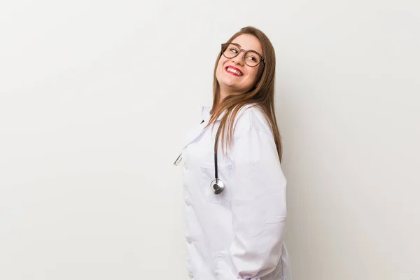 Jonge Dokter Vrouw Tegen Een Witte Muur Kijkt Opzij Glimlachend — Stockfoto