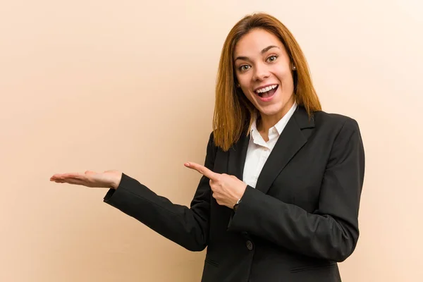 Young caucasian business woman excited holding a copy space on palm.