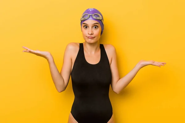 Young swimmer caucasian woman doubting and shrugging shoulders in questioning gesture.