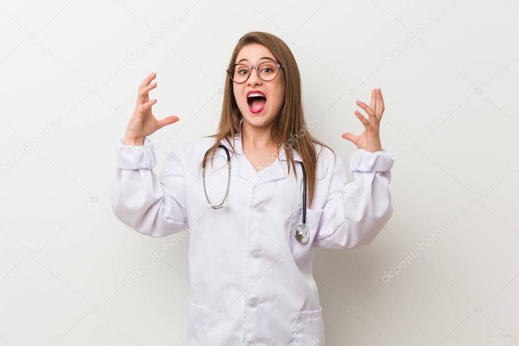 Young doctor woman against a white wall screaming with rage.