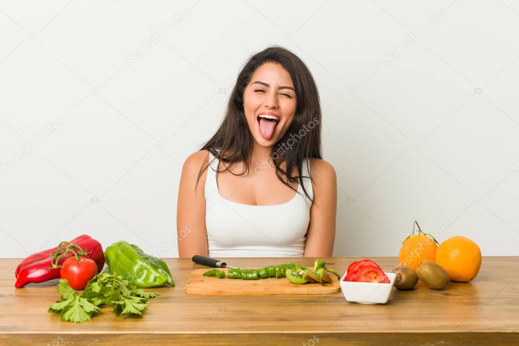 Young curvy woman preparing a healthy meal funny and friendly sticking out tongue.