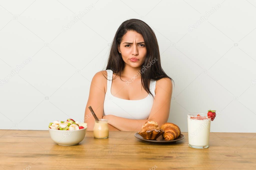 Young curvy woman taking a breakfast frowning face in displeasure, keeps arms folded.