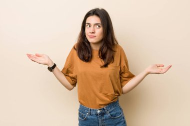 Genç esmer kadın bir bej arka plan şüphe karşı ve sorgulama jest omuzsat.