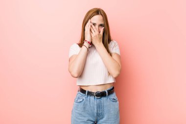Pembe bir duvara karşı genç kızıl saçlı zencefil kadın korkmuş ve sinirli parmakları ile göz kırpma.