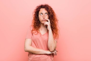 Genç doğal ve otantik kızıl saçlı kadın şüpheli ve şüpheci ifade ile yana bakıyor.