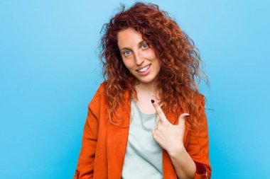 Young redhead elegant woman pointing with finger at you as if inviting come closer.