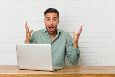 Genç filipinli adam bir zafer ya da başarı kutluyor onun laptop ile çalışan oturan, o şaşırır ve şok.