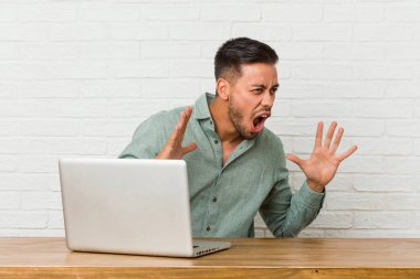 Dizüstü bilgisayarıyla çalışan genç filipinli adam yüksek sesle bağırır, gözleri açık tutar ve elleri gergin.