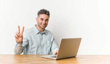 Genç yakışıklı adam parmakları ile iki numara gösteren dizüstü bilgisayar ile çalışıyor.