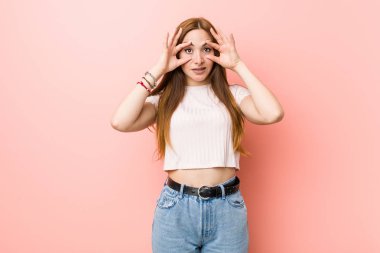 Genç kızıl saçlı zencefil kadın pembe bir duvara karşı gözleri bir başarı fırsatı bulmak için açık tutarak.