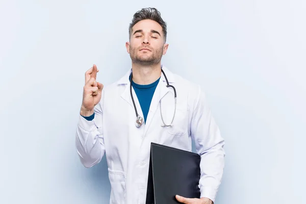 Caucasian Doctor Man Holding Folder Crossing Fingers Having Luck — Stock Photo, Image