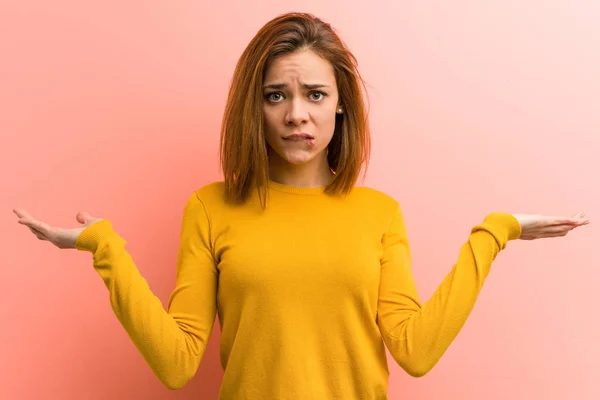 Young pretty young woman confused and doubtful raising her hands to hold a copy space.