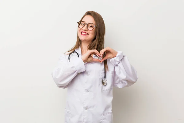 Jonge Dokter Vrouw Tegen Een Witte Muur Glimlachend Toont Een — Stockfoto