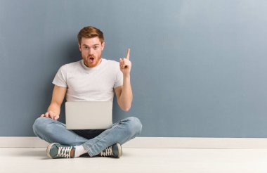 Genç kızıl saçlı öğrenci adam harika bir fikir, yaratıcılık kavramı sahip katta oturuyor. Elinde bir dizüstü bilgisayar var..