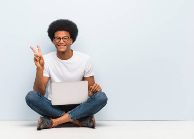 Genç siyah adam zafer bir jest yapıyor bir dizüstü bilgisayar ile katta oturan