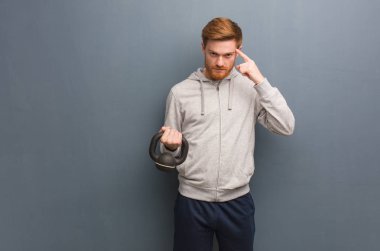 Genç kızıl saçlı fitness adamı bir fikir düşünüyor. Bir dambıl tutarak.