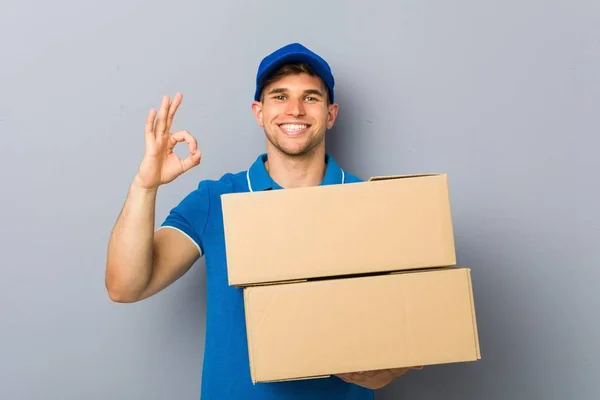 Jovem Entregando Pacotes Alegre Confiante Mostrando Gesto — Fotografia de Stock