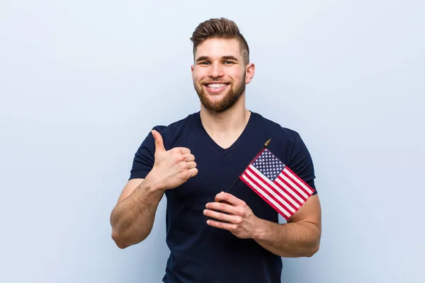 Young caucasian man holding a united states flag smiling and raising thumb up