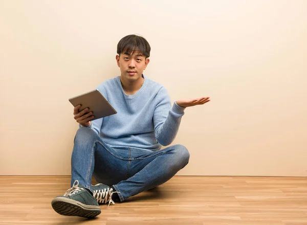 Young chinese man sitting using his tablet holding something with hands