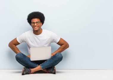 Genç siyah adam kalçalarında elleri ile bir dizüstü bilgisayar ile katta oturan