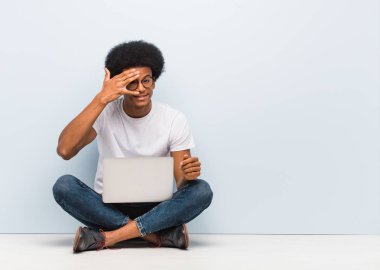 Genç siyah adam bir dizüstü bilgisayar ile katta oturan utandım ve aynı zamanda gülüyor