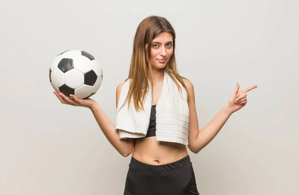 若いフィットネスロシアの女性は 指で側面を指しています サッカーボールを持っている — ストック写真