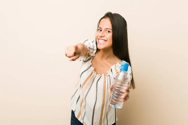 年轻的西班牙妇女拿着一瓶水欢快的微笑指向前面 — 图库照片